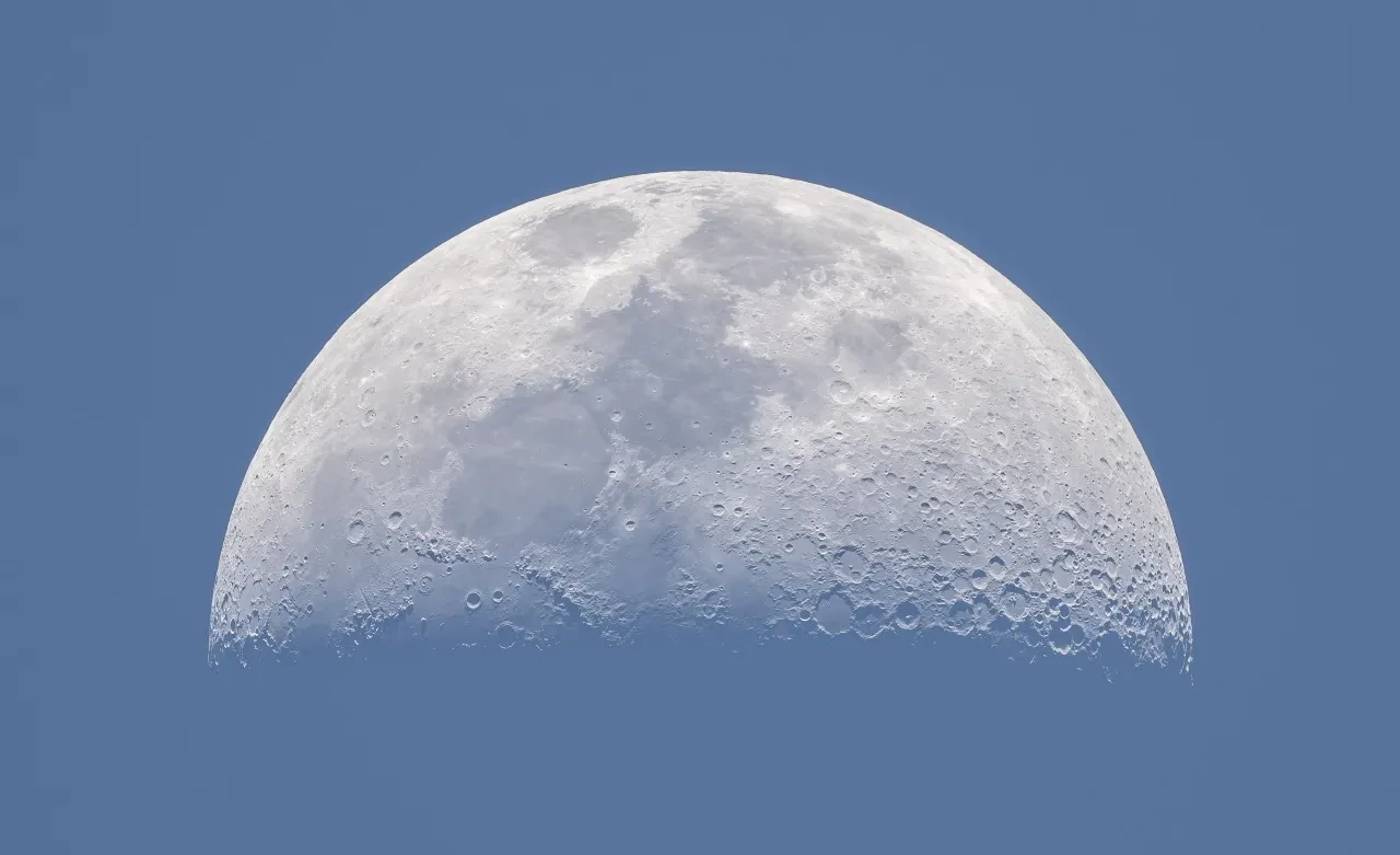 A horizontal cresent moon in a pale blue-grey sky.